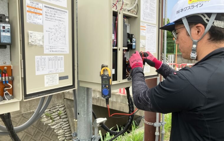ネクスラインの作業員が制御盤をクランプメーターで測定する様子