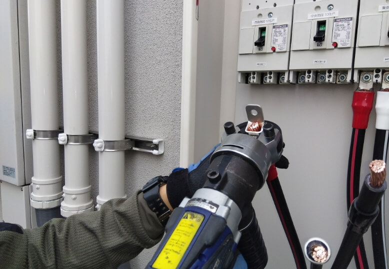 分電盤の内部で圧着工具を使い、電気配線の接続作業を行っている写真
