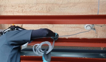 電動工具を使い、外壁に沿って金属配管の取り付け作業を行っている写真